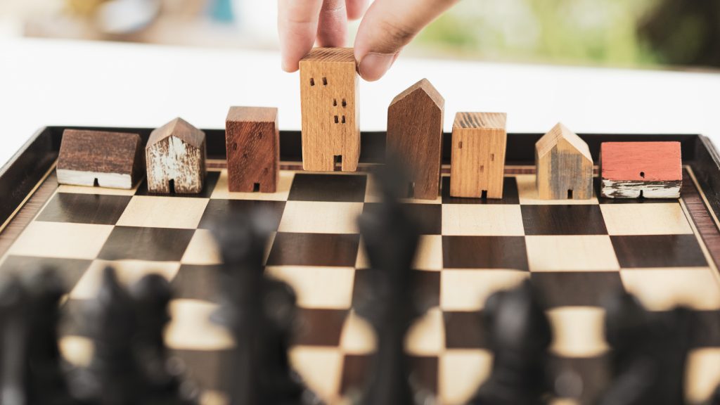Hand of business man moving chess to Building and house models in chess game, competition success play. strategy, management or leadership concept